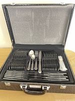 Open presentation case showing full 84-piece stainless steel flatware set neatly arranged