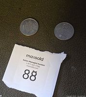 Two aluminum tokens front sides visible with torn lot number slip