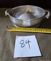 Front view showing casserole with lid, handles, and measuring tape for scale