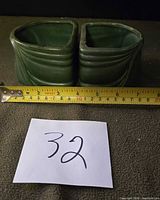 Two green ceramic planters side by side with tape measure for scale