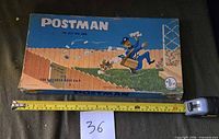 Closed box showing full lid artwork "POSTMAN The Jolly Mail Game" with tape for scale