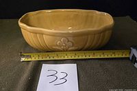 Front view showing amber glaze, ribbed sides, floral motif, tape for length