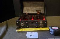 Front view of open chest showing decanters and shot glasses with tape measure for scale