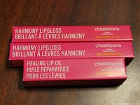 Front view of three boxed lip products: two Harmony Lipgloss and one Sustain lipstick