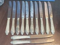 All twelve ornate silver plate knives front view
