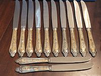 Full set of twelve ornate silver-plate knives with two shown horizontally for detail