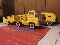 Side view of the vintage yellow Tonka metal cab truck with two rear attachments on a wooden floor