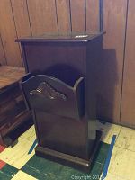 Side view of wood side table showing basket slot for magazines with carved decorative design