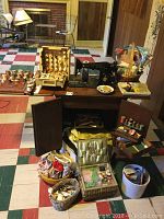 Overview photo showing vintage Singer sewing machine sitting on collapsible wooden table with multiple baskets and holders containing sewing accessories such as threads, scissors, measuring tape, and fabrics.