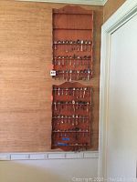 Two wooden wall-mounted spoon display racks filled with a variety of silver spoons hanging on a beige textured wall.