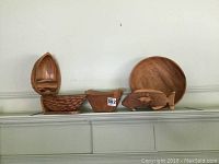 Photo of shelf displaying wooden decor items: a boat shaped carved sculpture with textured scales, walnut shaped box with lid, a round wooden bowl, and carved wooden fish figurine.