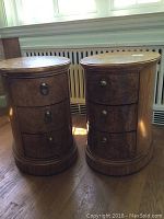Front view of two oval wooden end tables with three drawers each, showing metal ring handles and some wear.