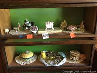 Shelf with assorted trinkets and decorative pieces arranged on lace doilies, including a bunny figurine, floral china, and jewelry pieces.