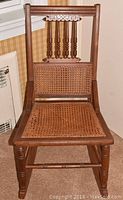 Front view of the wooden rocking chair showing woven cane seat and carved wooden backrest.