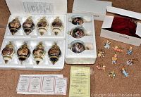 Photo showing eight Bradford Editions collector ornaments in original styrofoam packaging, with certificates in background, and five Hummel baby angel figures beside them.