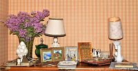 Wide view of all decor items including lamps, framed prints, vase with flowers and figurines on a shelf against plaid wallpaper