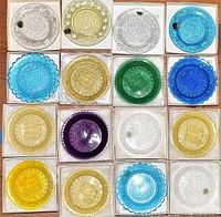 Top view photo of 16 assorted lead crystal bicentennial cup plates in various colors, displayed in or near their original boxes.