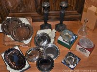 Lot overview showing all silver plated serving items, crystal bowl, and additional plates with candlesticks in the background.