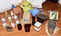 Photo shows the assortment of two ceramic teapots, red glass cups, ceramic dwarfs, decorative plates, and vintage charcoal iron with box.