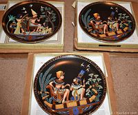 Three Osiris porcelain plates laid out on a surface, showing the detailed Egyptian-themed designs on black backgrounds with gold edging and original certificates underneath.