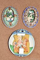 Three Bradford Exchange decorative plates: two oval floral plates with gold detailing and one round carousel horse plate with child figure