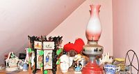 Wide view showing assorted decorative items including figurines, framed artwork, vases, and a glass hurricane lamp on a shelf against a pink wall.