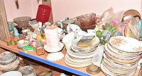 Full view of assorted teacups, saucers, plates, candle holders, figurines and other decorative items stacked on shelving unit.