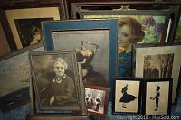 Photo showing a collection of framed vintage prints and portraits leaning against a surface; varied subject matter including portraits, landscapes, and floral prints