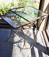 Two square glass top side tables with metal frames showing rust. Photos capture the decorative curved metal scroll designs and clear glass tops. The tables appear weathered and worn.
