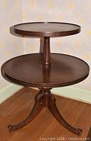 Full side view of round 2 tier wooden table showing shape, finish and legs