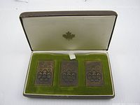 Open case showing three bronze replica stamps on green velvet base