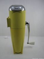 Left side profile of yellow ice crusher showing crank handle and overall form