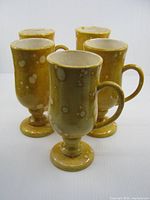 Five yellow speckled ceramic pedestal mugs, front view