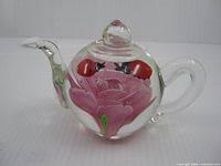 Side view showing clear glass teapot form, pink flower and two ladybugs