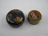 Two small round containers side by side: painted powder tin left, micro mosaic pill box right