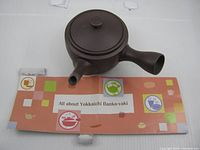 Top and side view of brown clay kyusu with folded leaflet