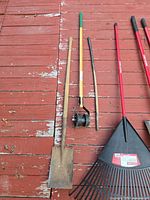 Left-side tools: wood-handle shovel, two-wheel line reel, wood-handle bow rake