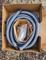 coiled corrugated vacuum hose with small bagged parts in box