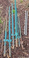 Group of teal/green and rusted steel fence posts laid on ground