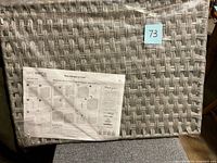 Front of sealed grey woven hamper package showing texture and instruction sheet