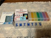 All four pill organizers: two boxed MEDca products, rainbow pill case, clear case with blue letters