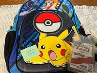 Front view of Pokémon backpack showing Pikachu graphic, Poké Ball design, attached sealed card pack