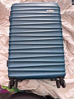 Front view of ribbed teal Akslvision suitcase with four double-spinner wheels