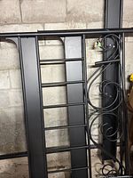 Disassembled black metal bed frame showing decorative scroll head/footboard, side rails