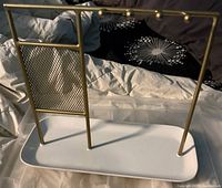 Overall view of gold metal jewelry hanger on white tray base
