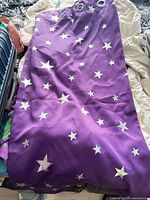 Purple curtain panel with silver star print and metal grommets displayed on bed