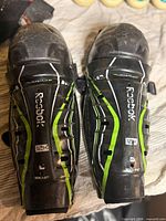 Front view of both Reebok 12K youth shin pads showing branding, graphics and overall wear