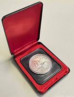 Closed black presentation case opened to show coin in capsule