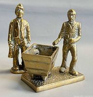 Front view of both brass miner figurines and mine cart