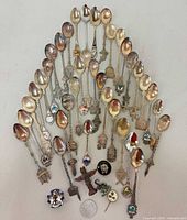 Full group of souvenir teaspoons arranged in fan shape with pins and coin at bottom
